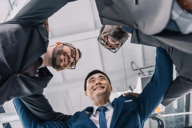 Vue en contre-plongée de trois hommes d'affaires d'origines diverses se tenant par les épaules pour illustrer le leadership interculturel.